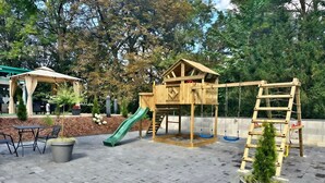 Un parque infantil con un tobogán de madera, columpios y una estructura para escalar.