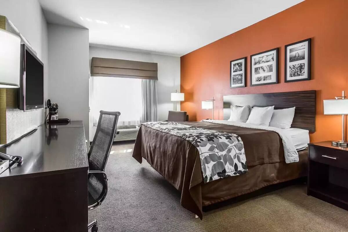 A hotel room with a bed, desk, chair, and a TV.