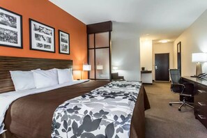 A hotel room with a large bed, a desk, and a chair. There are framed pictures on the wall and a sliding door leading to another room.