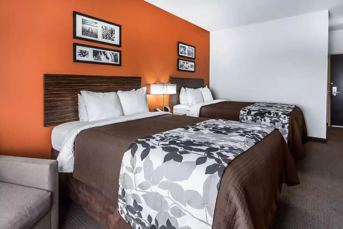A hotel room with two beds, a nightstand, a lamp, and framed pictures on the wall.