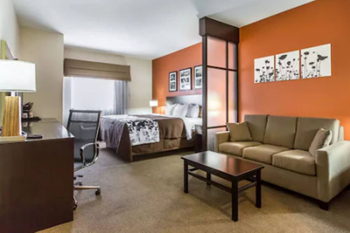 A hotel room with a bed, a sofa, a desk, and a chair. There are wall art pieces and a window with curtains.