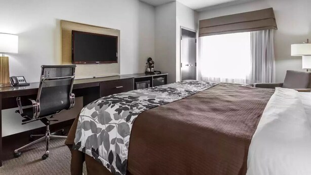 A hotel room with a large bed, a desk with a chair, a flat-screen TV, and a window with curtains. - Sleep Inn & Suites Lubbock West (Lubbock)
