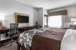 A hotel room with a large bed, a desk with a chair, a flat-screen TV, and a window with curtains.