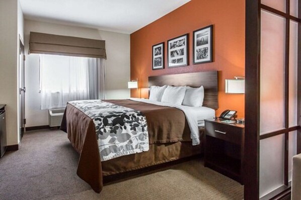 A hotel room with a large bed, a bedside table with a lamp, a window with curtains, and framed pictures on the wall.