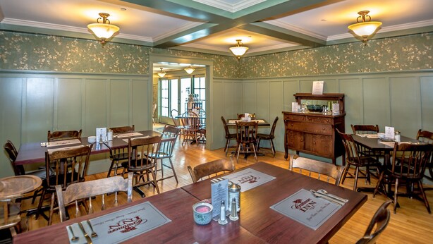 Un comedor con mesas y sillas de madera, un aparador de madera y apliques decorativos.