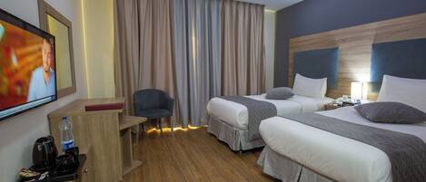 A hotel room with two beds, a desk with a chair, a TV, and a minibar.