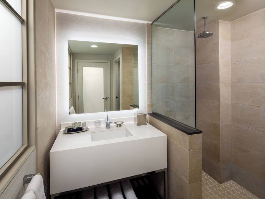 Un baño moderno con un tocador blanco, un espejo grande y una zona de ducha con mampara de vidrio.