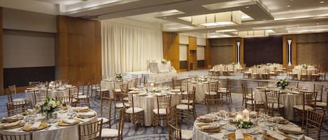 Un amplio salón de banquetes con varias mesas redondas dispuestas para el servicio de comidas, organizado en un espacio diáfano con techos altos e iluminación moderna.