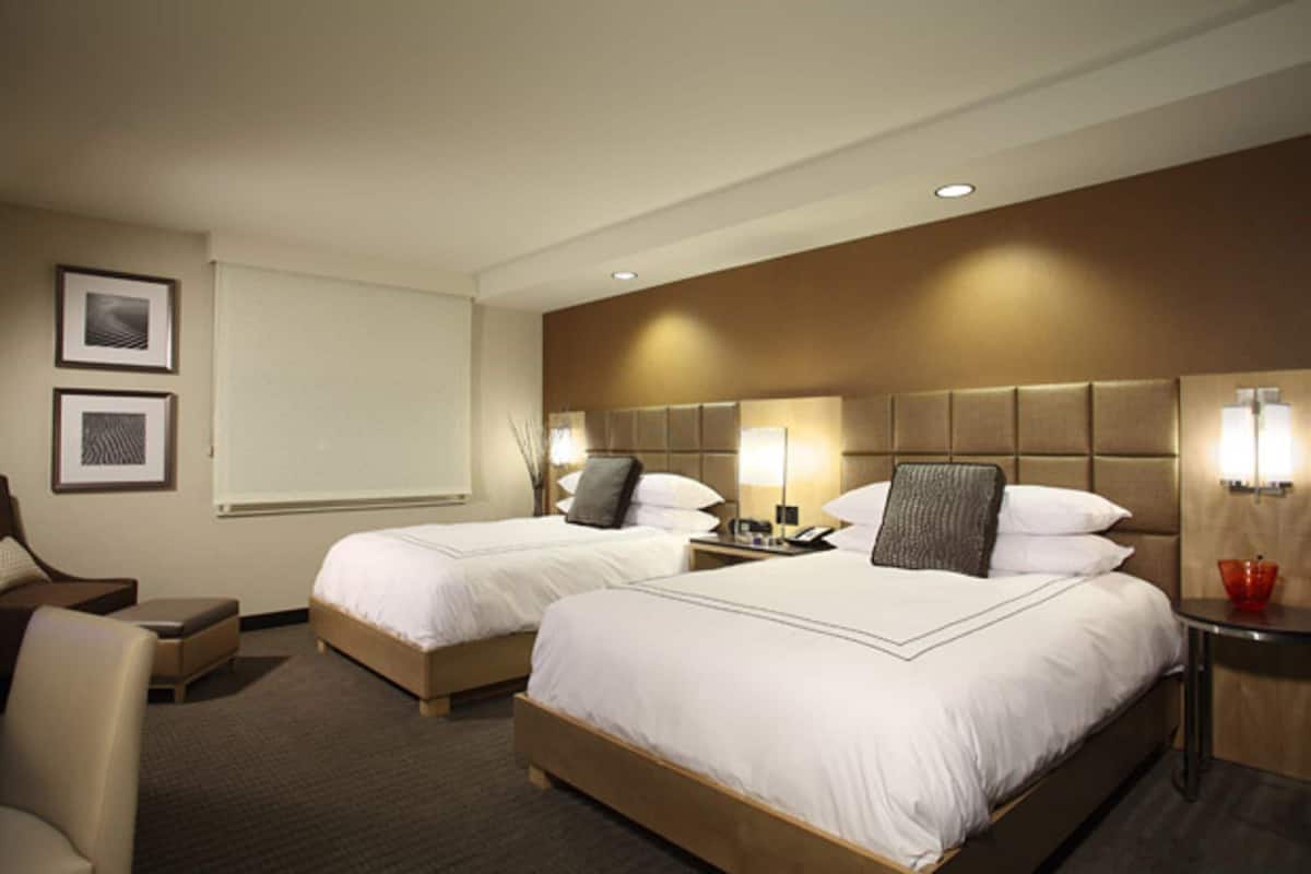 A hotel room with two beds, a desk, a chair, and a small table.