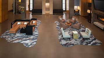A modern lobby with a seating area featuring sofas and armchairs, a fireplace, and a television.