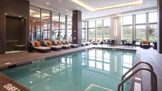 A modern indoor swimming pool with lounge areas and large windows. - The Hotel at Arundel Preserve (Hanover)