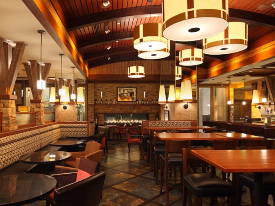 A restaurant interior with wooden beams, round tables, and hanging pendant lights.