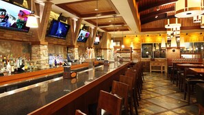 A bar area with a long counter, multiple TVs mounted on the wall, wooden chairs, and a tiled floor. - The Hotel at Arundel Preserve (Hanover)