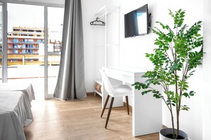 Una habitación de hotel moderna con un ventanal grande, un escritorio, una silla, un televisor y una planta en maceta.