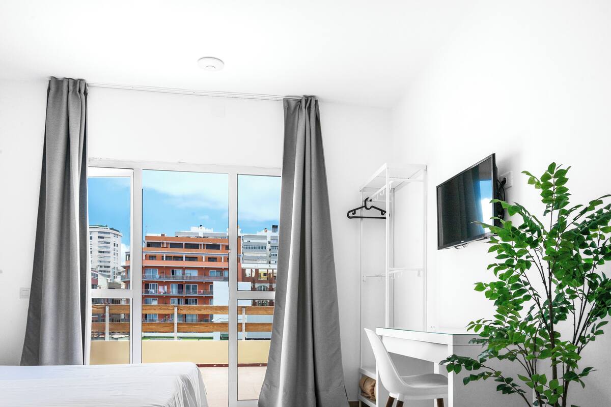 Una habitación de hotel con un ventanal grande, un escritorio, una silla y un televisor.