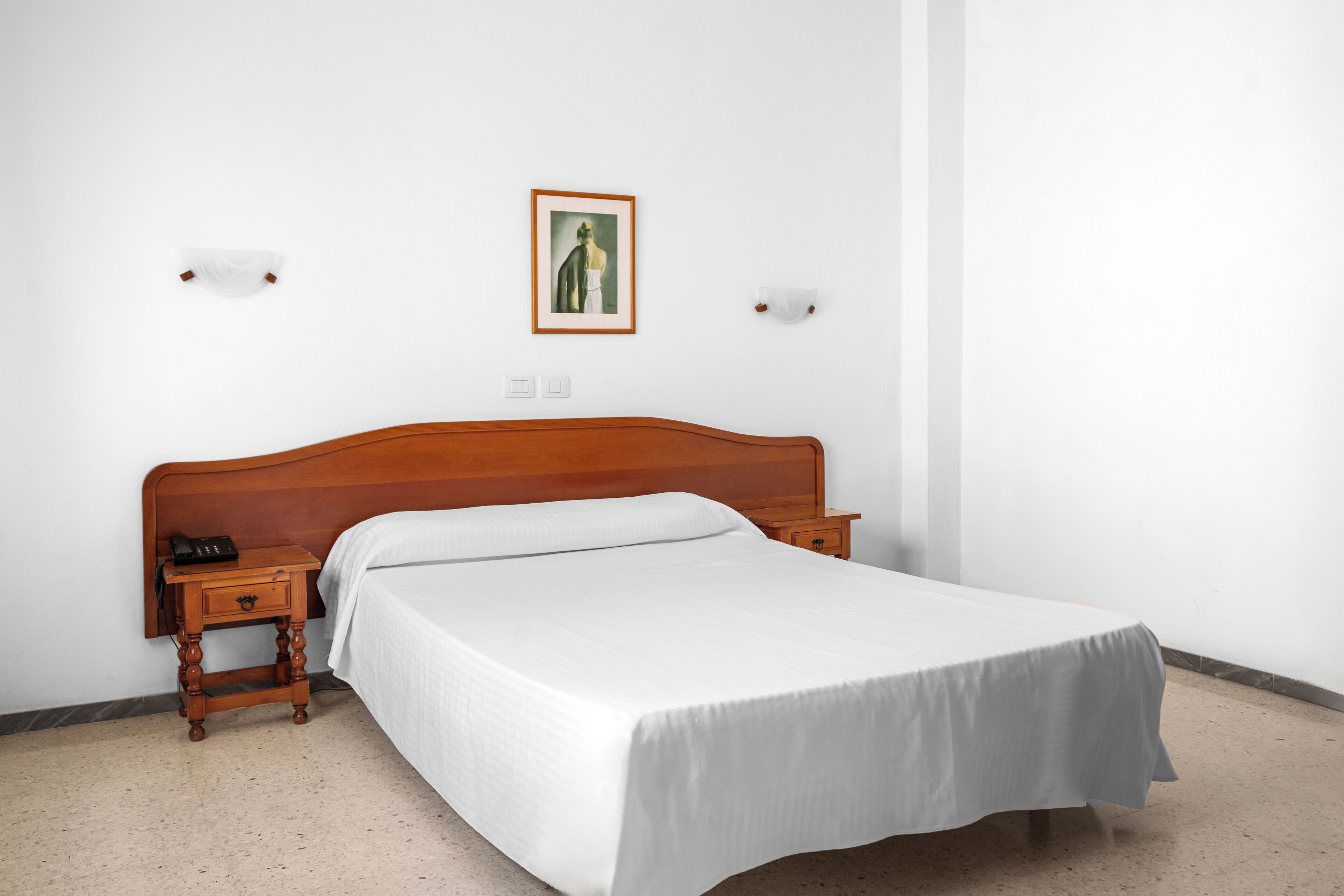 Un lit simple avec une tête de lit en bois, une table de chevet avec une lampe et un tableau encadré au mur.