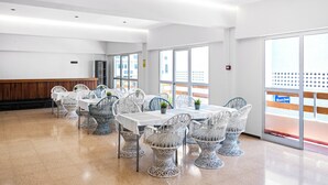 Un vaste espace dédié à la salle à manger, avec des tables et des chaises blanches, de grandes fenêtres et un comptoir en bois.