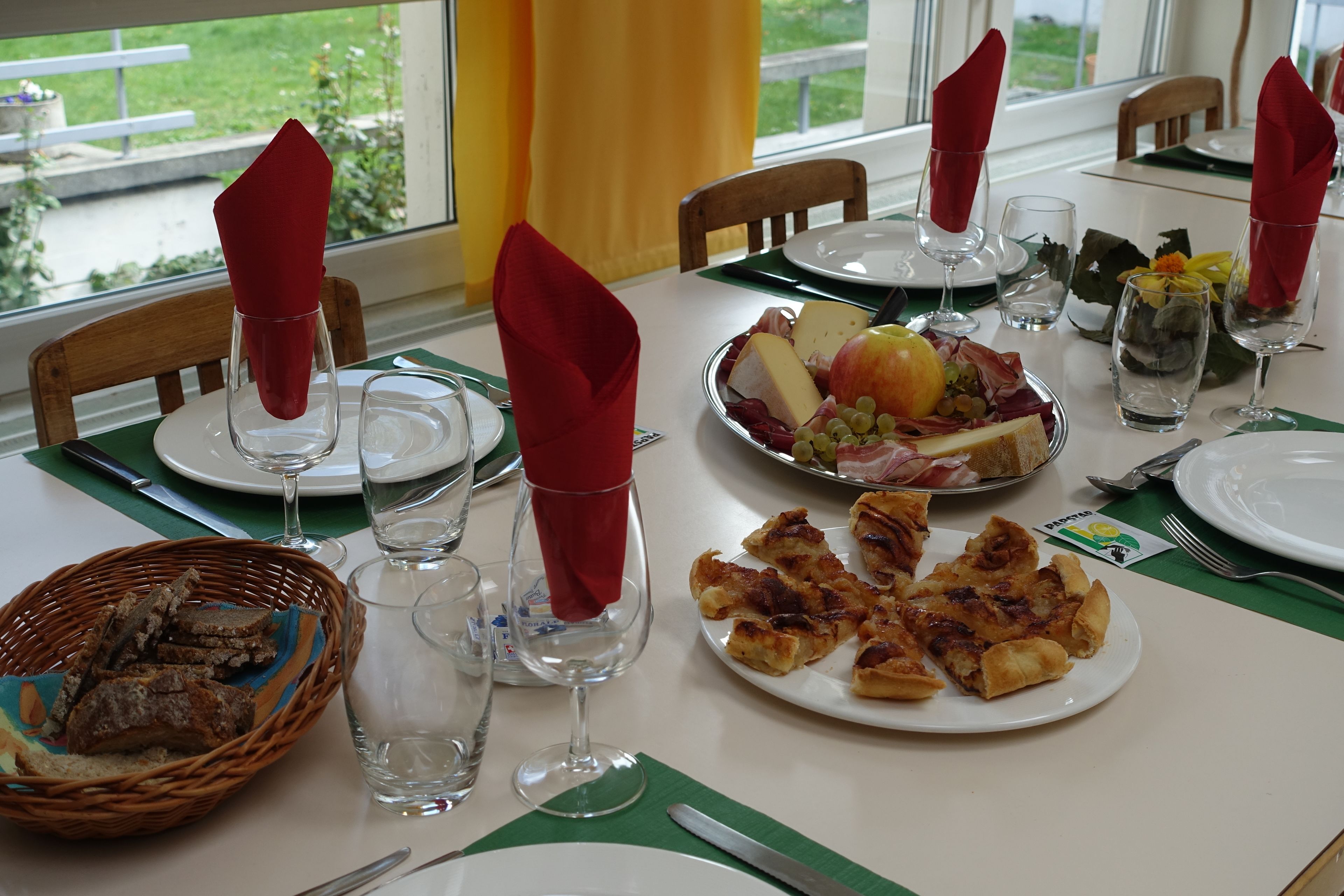 Una mesa de comedor puesta con platos, vasos y una cesta de pan.