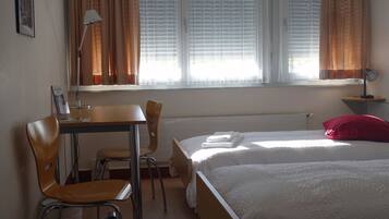 A hotel room with two beds, a desk, a chair, a lamp, and a window with curtains.