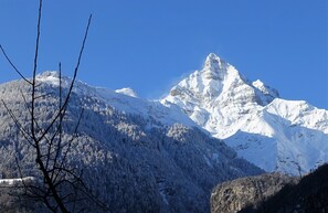 Una montaña nevada con un pico destacado, rodeada de bosque denso y terreno rocoso.