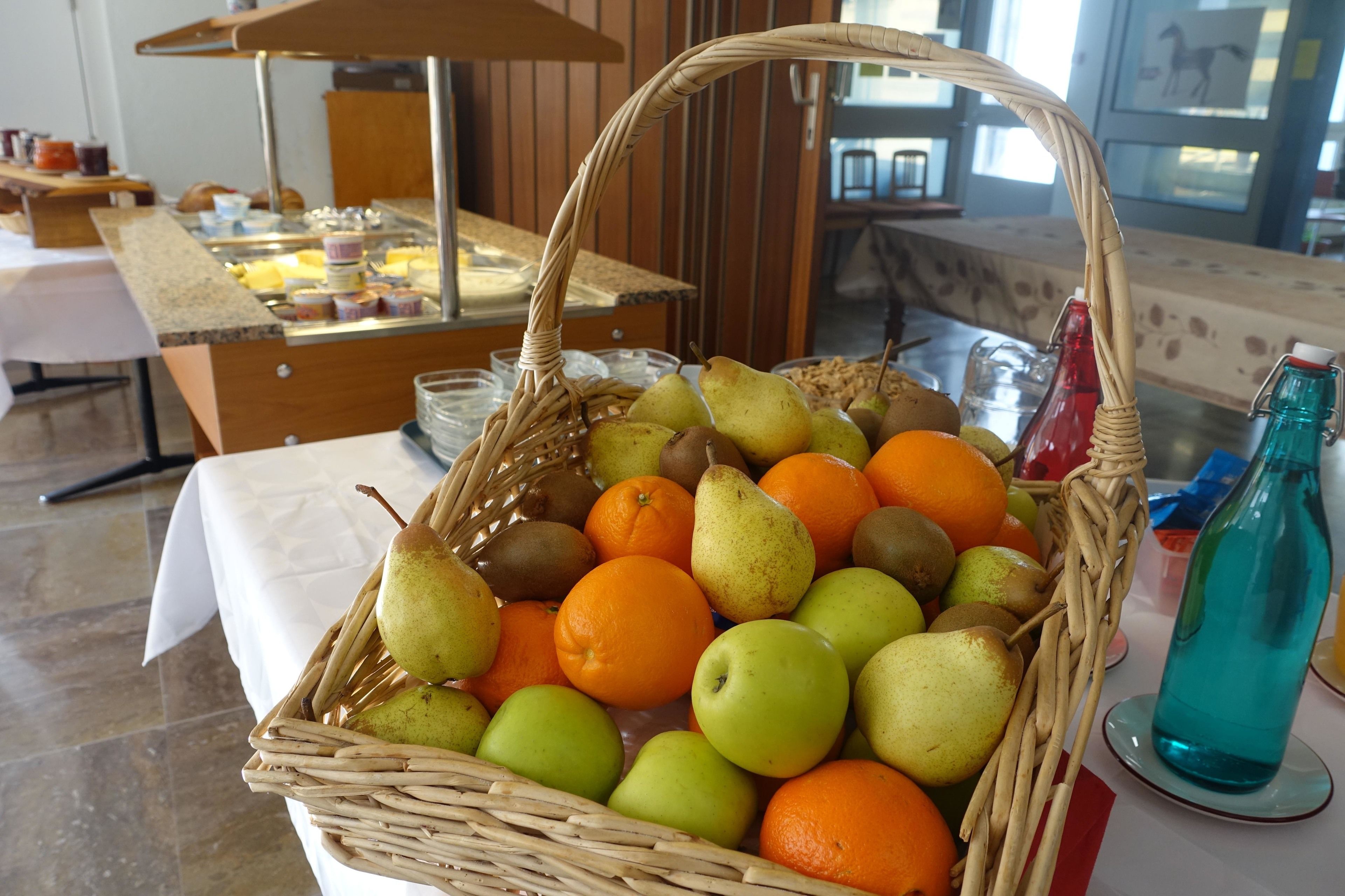 A fruit basket with pears, oranges, and apples on a table.