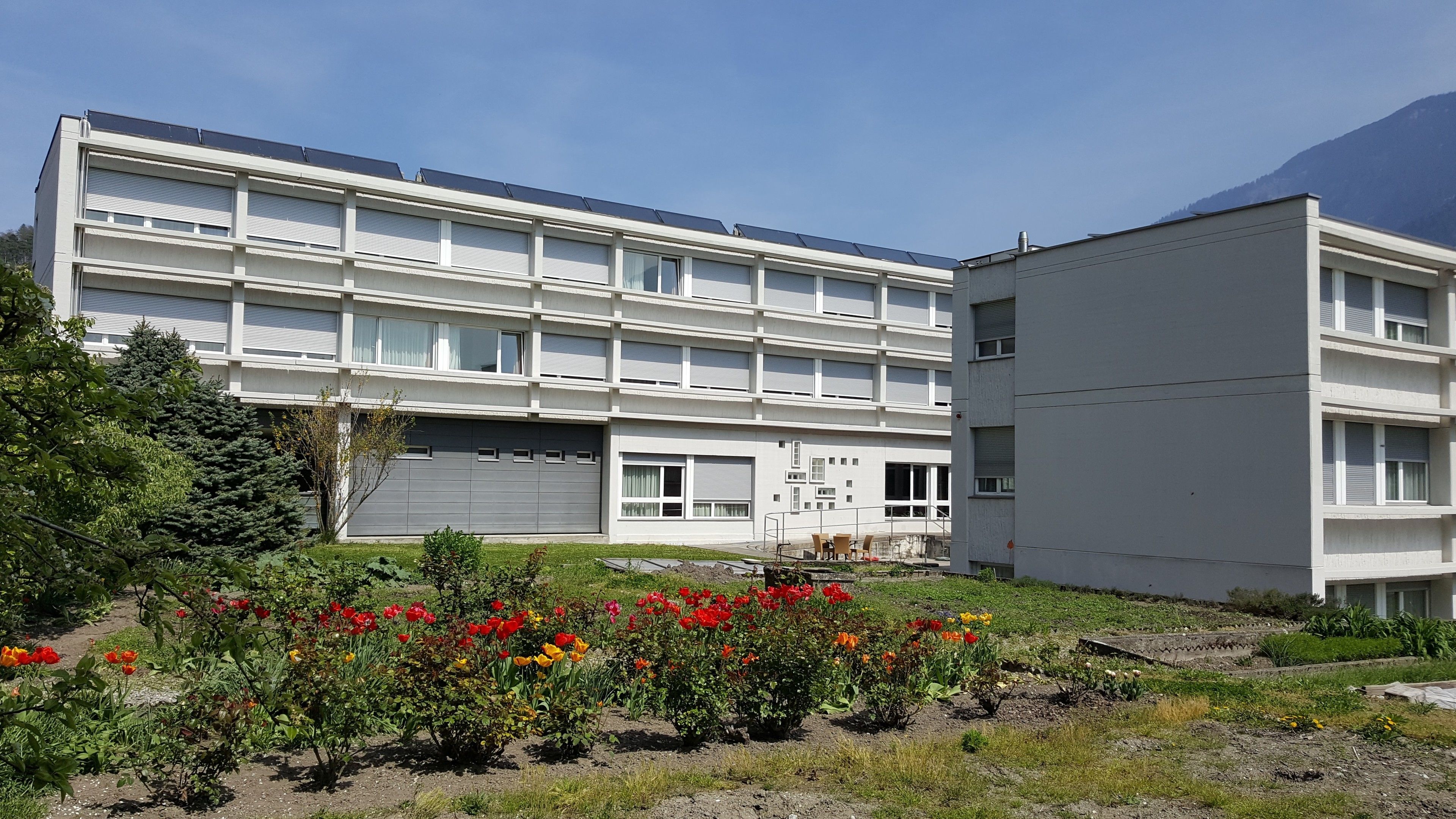 A modern building with multiple floors, large windows, and solar panels on the roof.