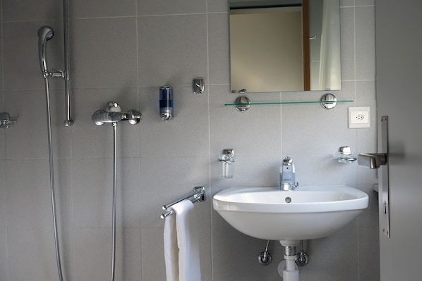 Un baño moderno con un lavamanos blanco, un estante de vidrio encima y un cabezal de ducha de mano, además de un perchero.