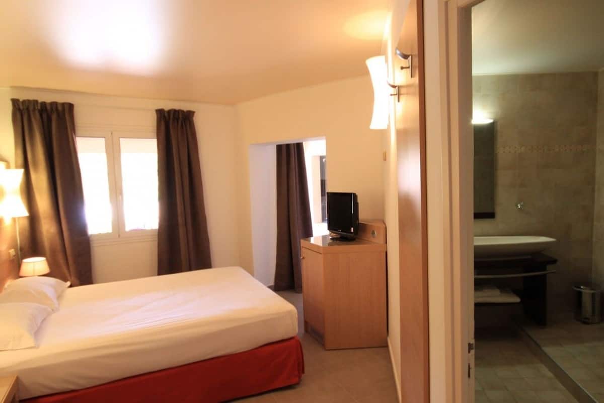 A hotel room with a bed, a TV on a wooden cabinet, a bathroom with a bathtub, and a sink.