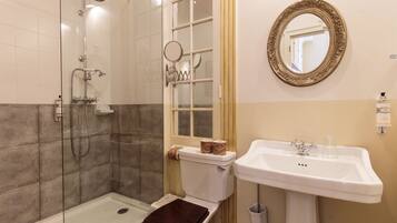 A bathroom with a glass-enclosed shower, a toilet with a brown seat, a sink with a faucet, and a mirror with an ornate frame.