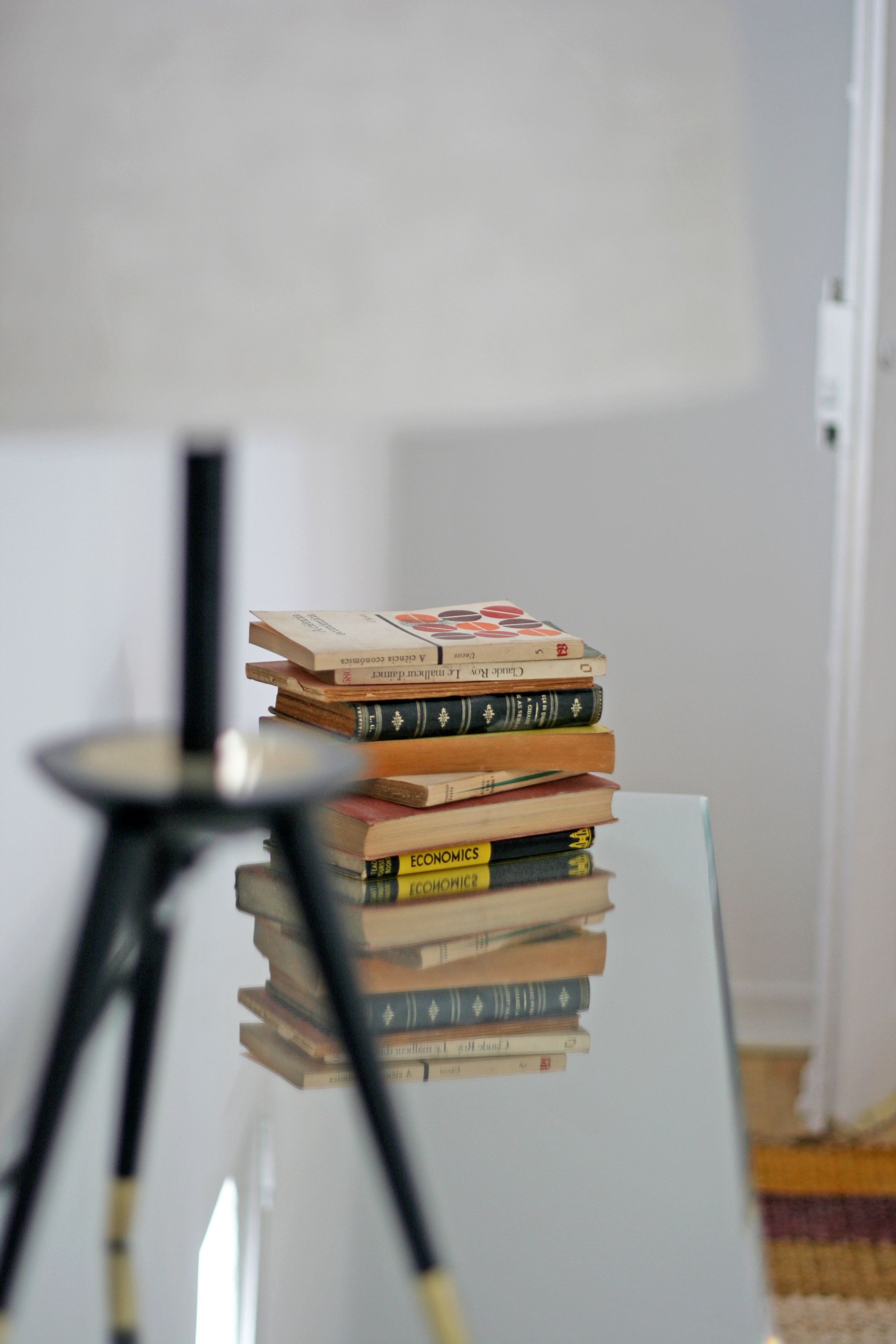 A stack of books on a glass table with a lamp in the foreground.
