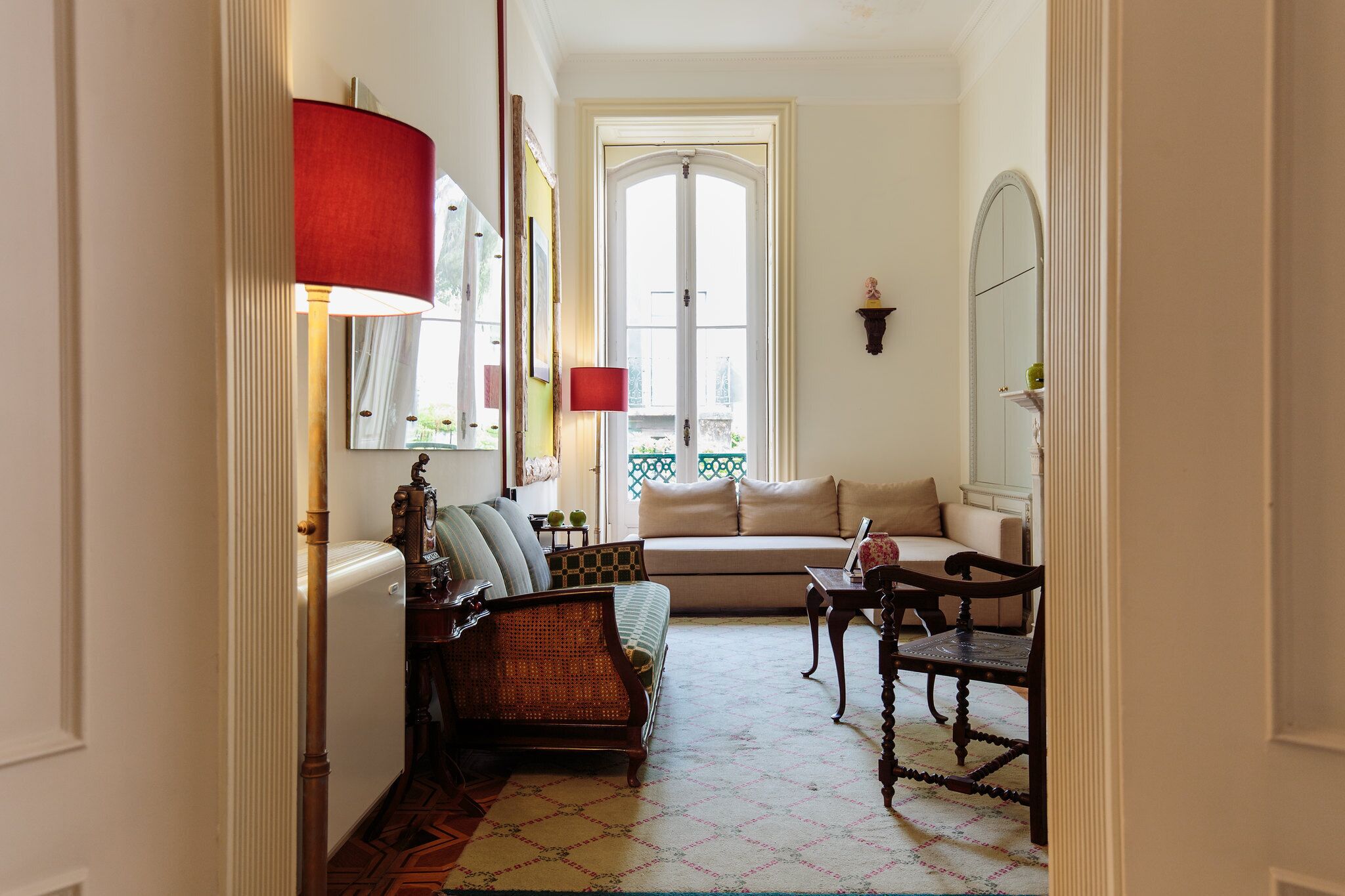 A room with a sofa, a chair, a lamp, a mirror, and a window.