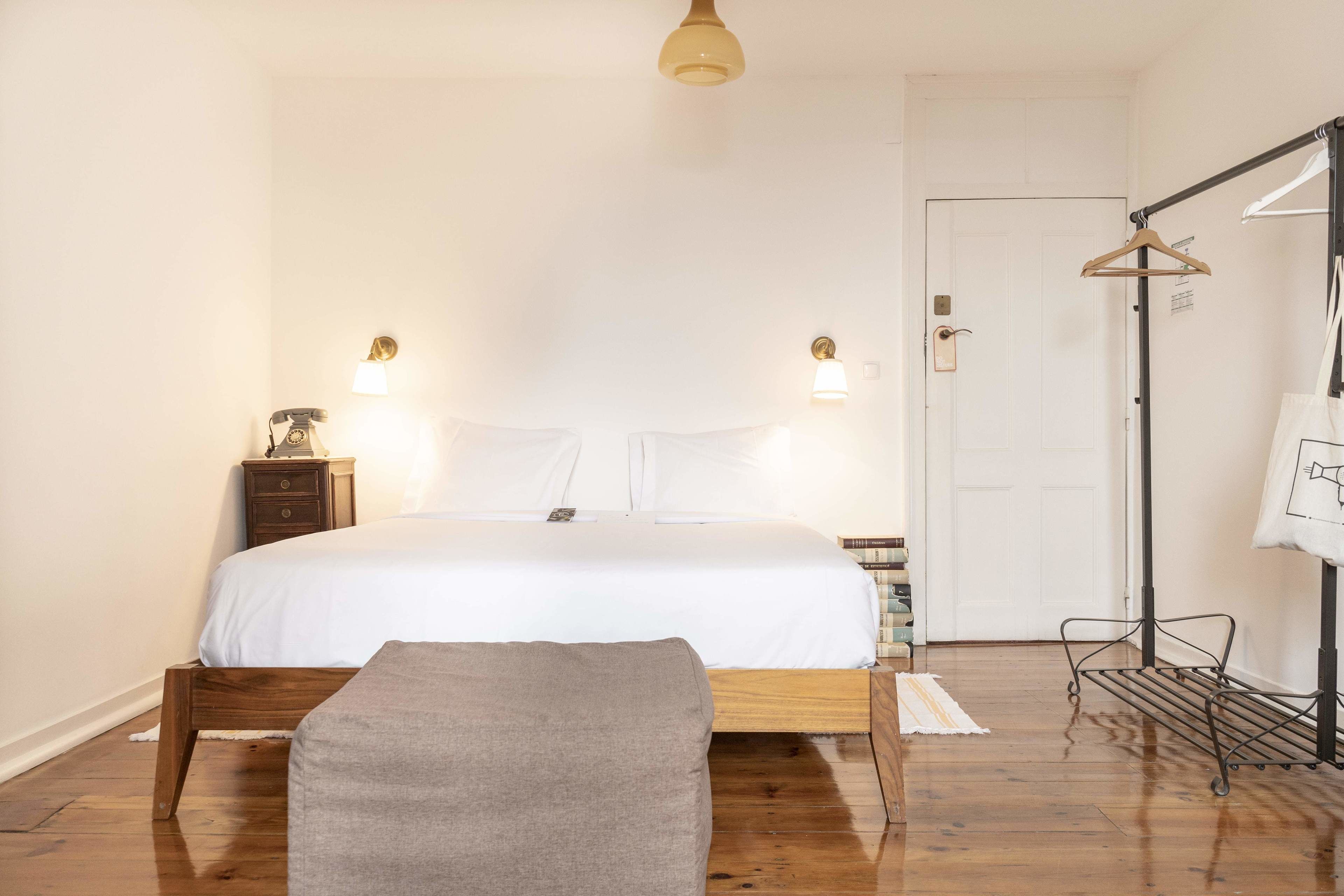 A bedroom with a wooden bed, bedside tables, a bench, a hanging clothes rack, and a door.