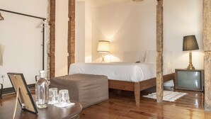 A bedroom with a bed, bedside lamp, wooden floor, and a small table with glasses and a bottle. - Independente Príncipe Real (Lisbon)