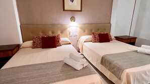 Habitación de hotel con dos camas, cada una con cabecera, mesita de noche y lámpara de pared.