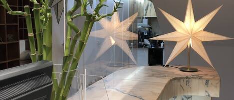 Una recepción con encimera de mármol, una planta de bambú en un florero transparente y dos lámparas con forma de estrella iluminadas.