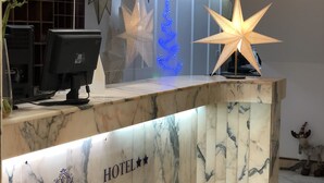 Una recepción de hotel con detalles de mármol, un letrero que dice "ATLANTICO CENTRO HOTEL", luces decorativas en forma de estrella y un monitor de computadora.