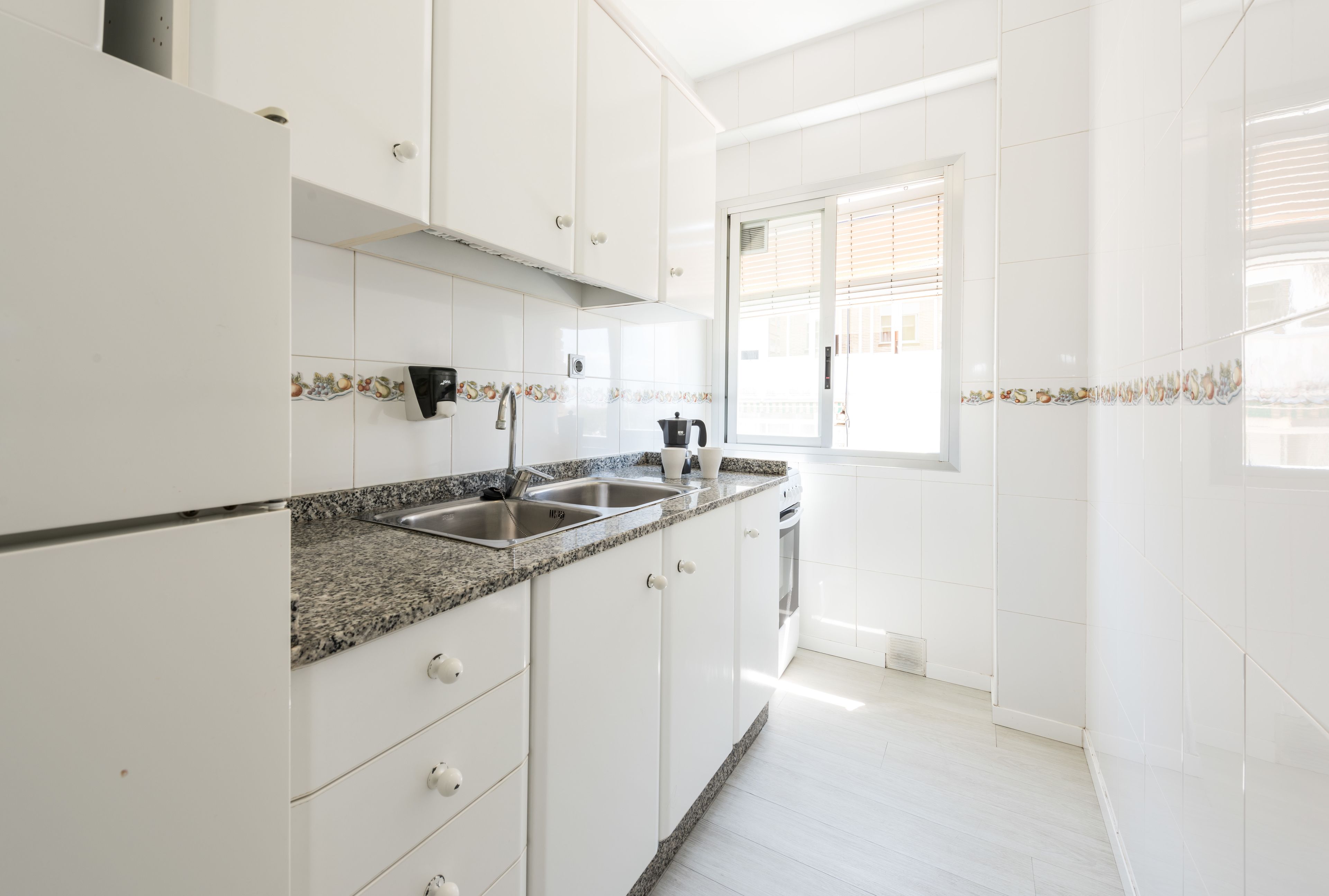 A modern kitchen with white cabinets, granite countertops, and a window with blinds.