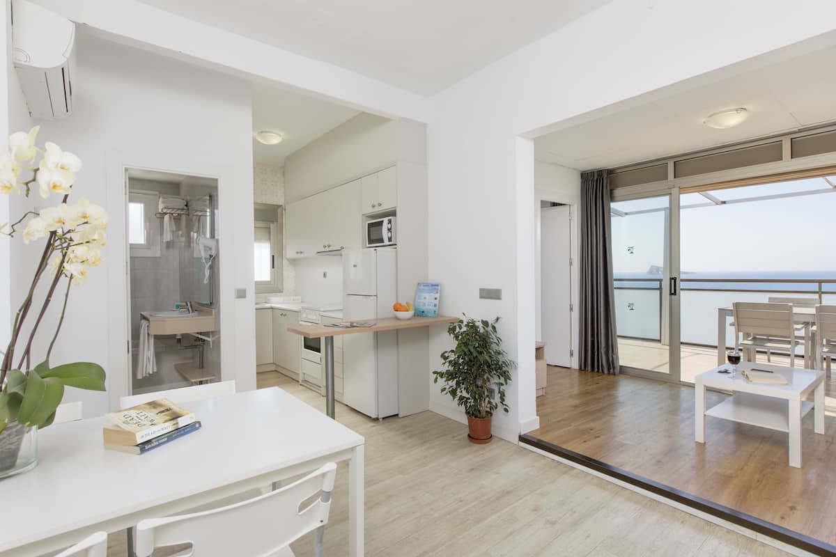 A modern kitchen with white appliances, a dining area with a table and chairs, and a balcony with a view.