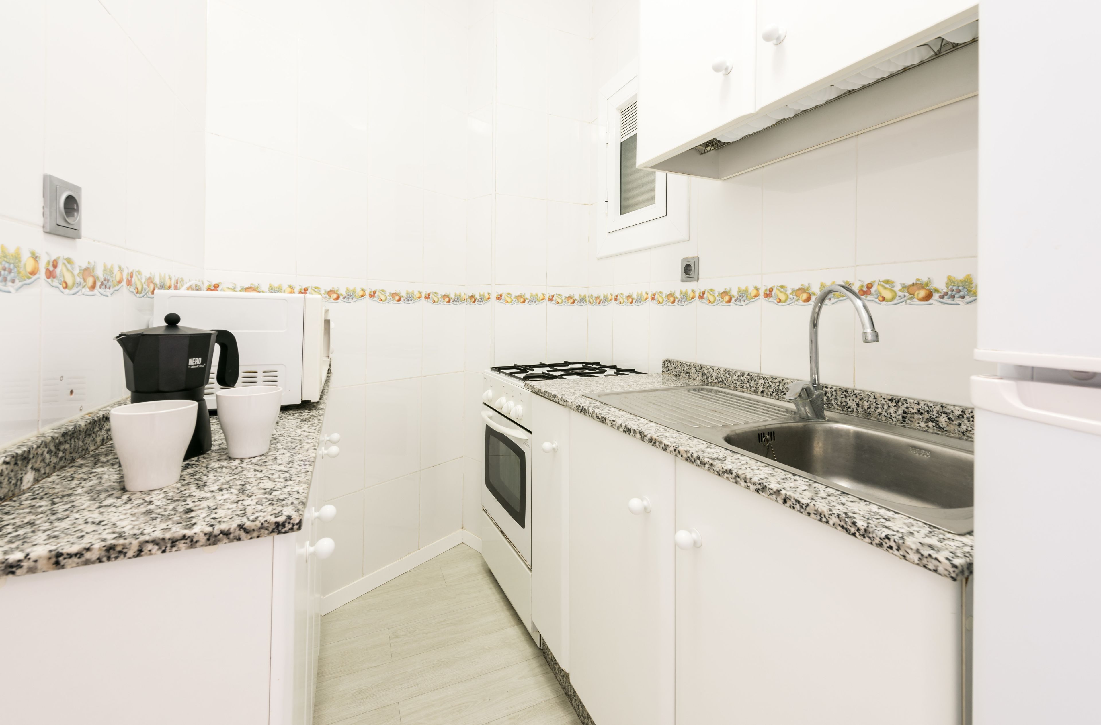 A small kitchen with white cabinets, a granite countertop, a stove, a sink, and a coffee maker.