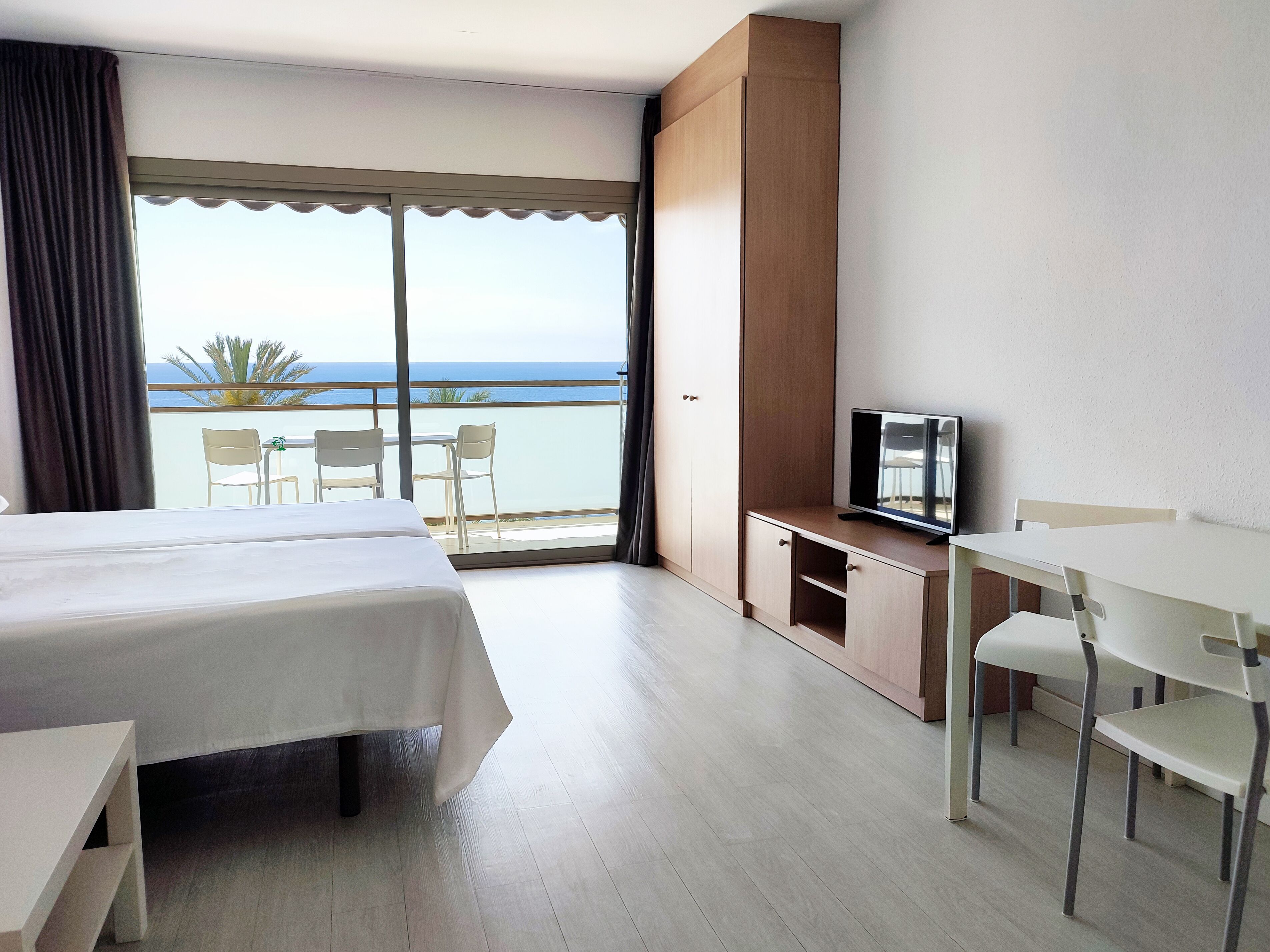 Ein Hotelzimmer mit Bett, Fernseher, Schreibtisch und einem Balkon mit Meerblick.