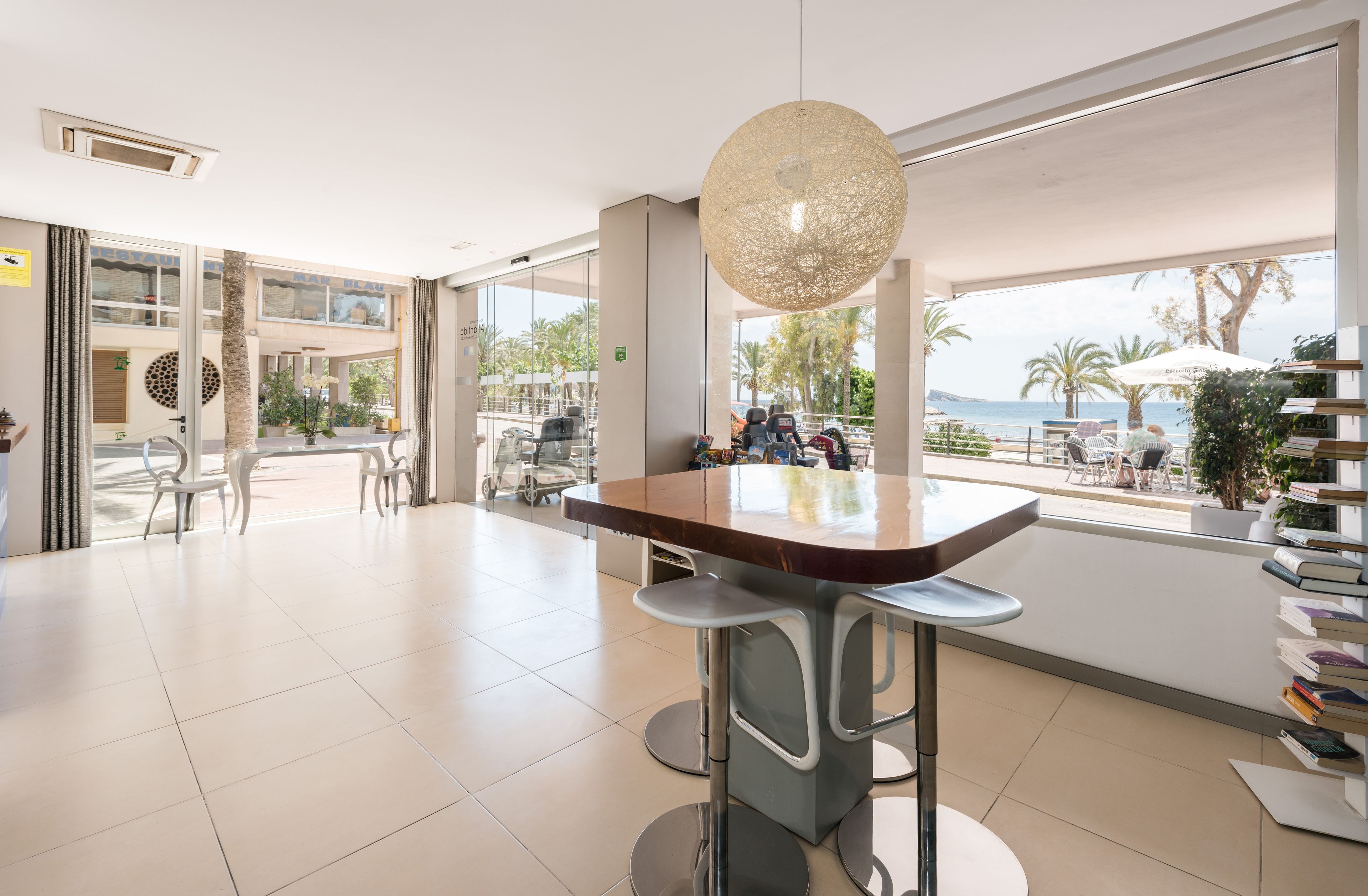 A modern indoor area with a bar, seating, and large windows overlooking a beach.