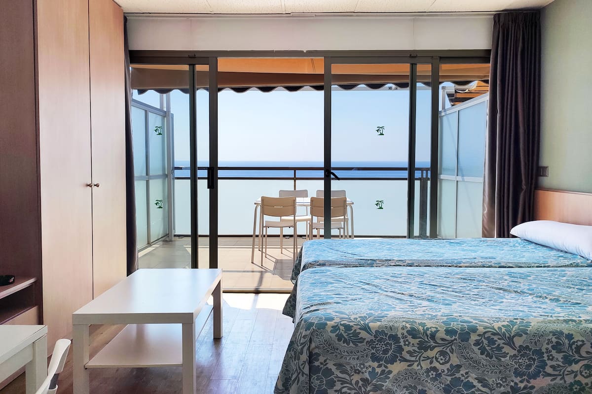 A hotel room with a balcony, a bed with a patterned bedspread, a small table, and two chairs.