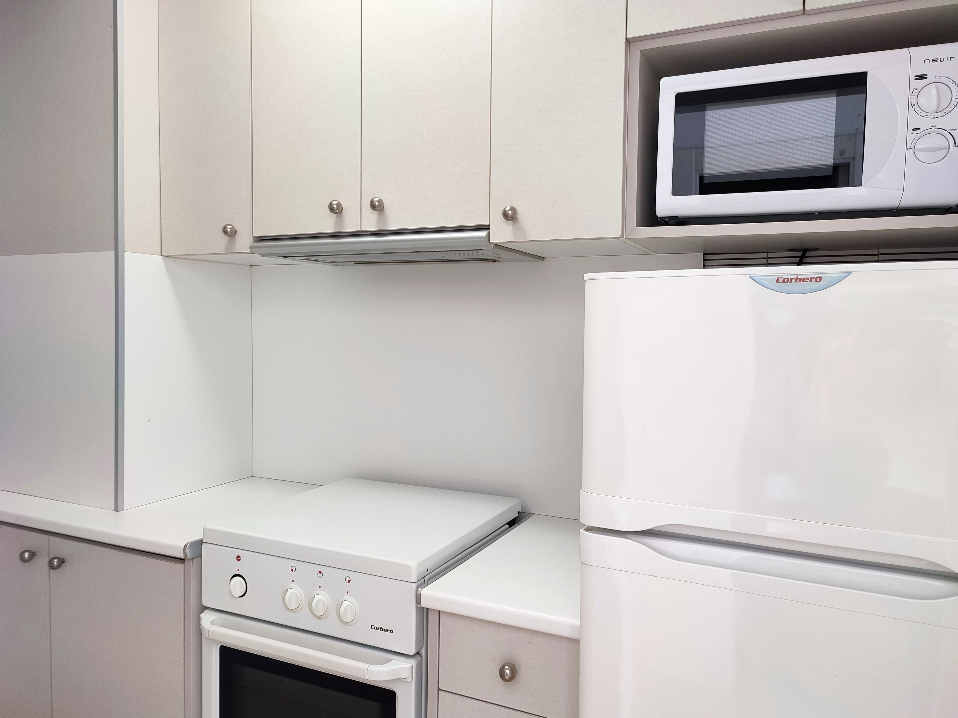 Una cocina con microondas, horno y un refrigerador Corbero.