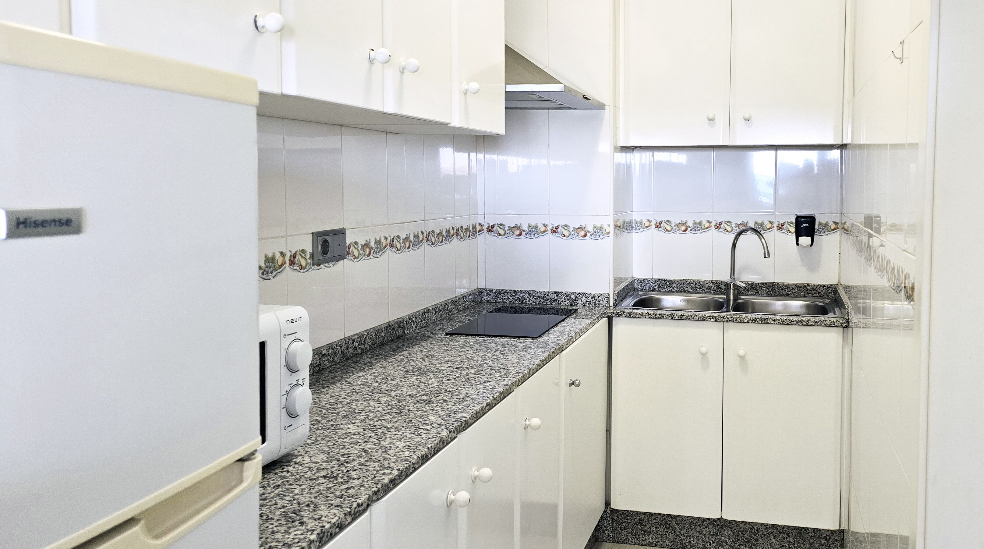 Una cocina compacta con armarios blancos, encimera de granito, pileta integrada y un tostador.