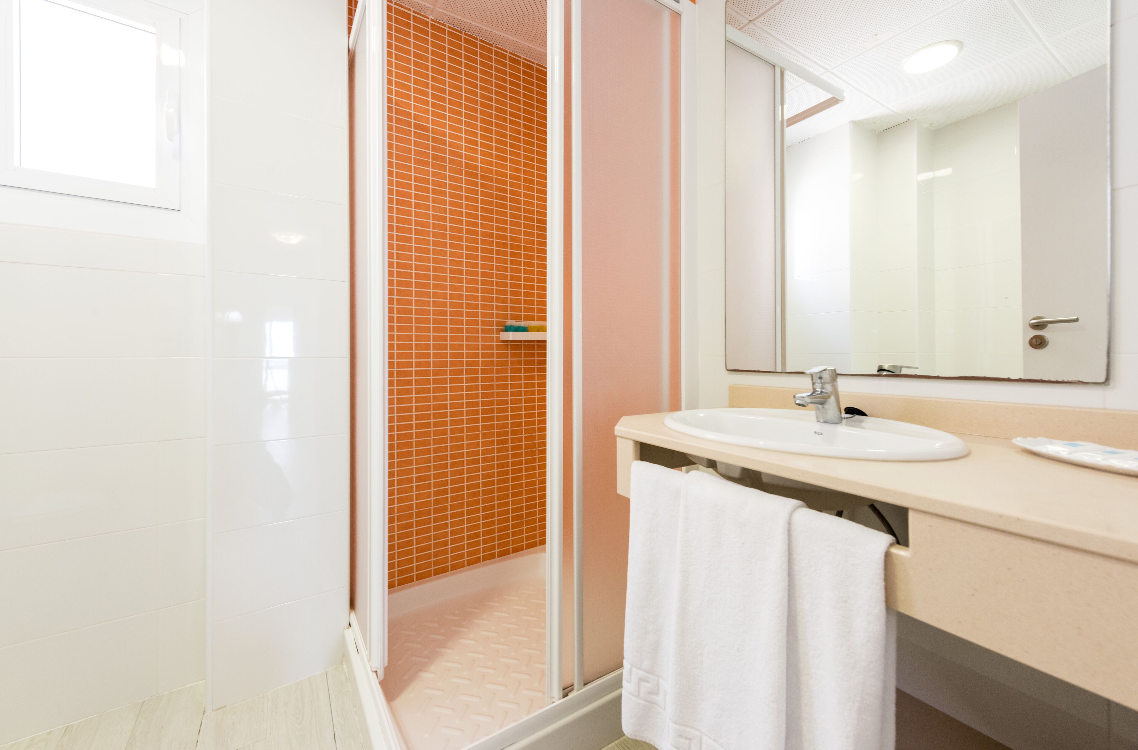 Une salle de bain moderne avec un lavabo blanc, un miroir et une douche aux carreaux orange.