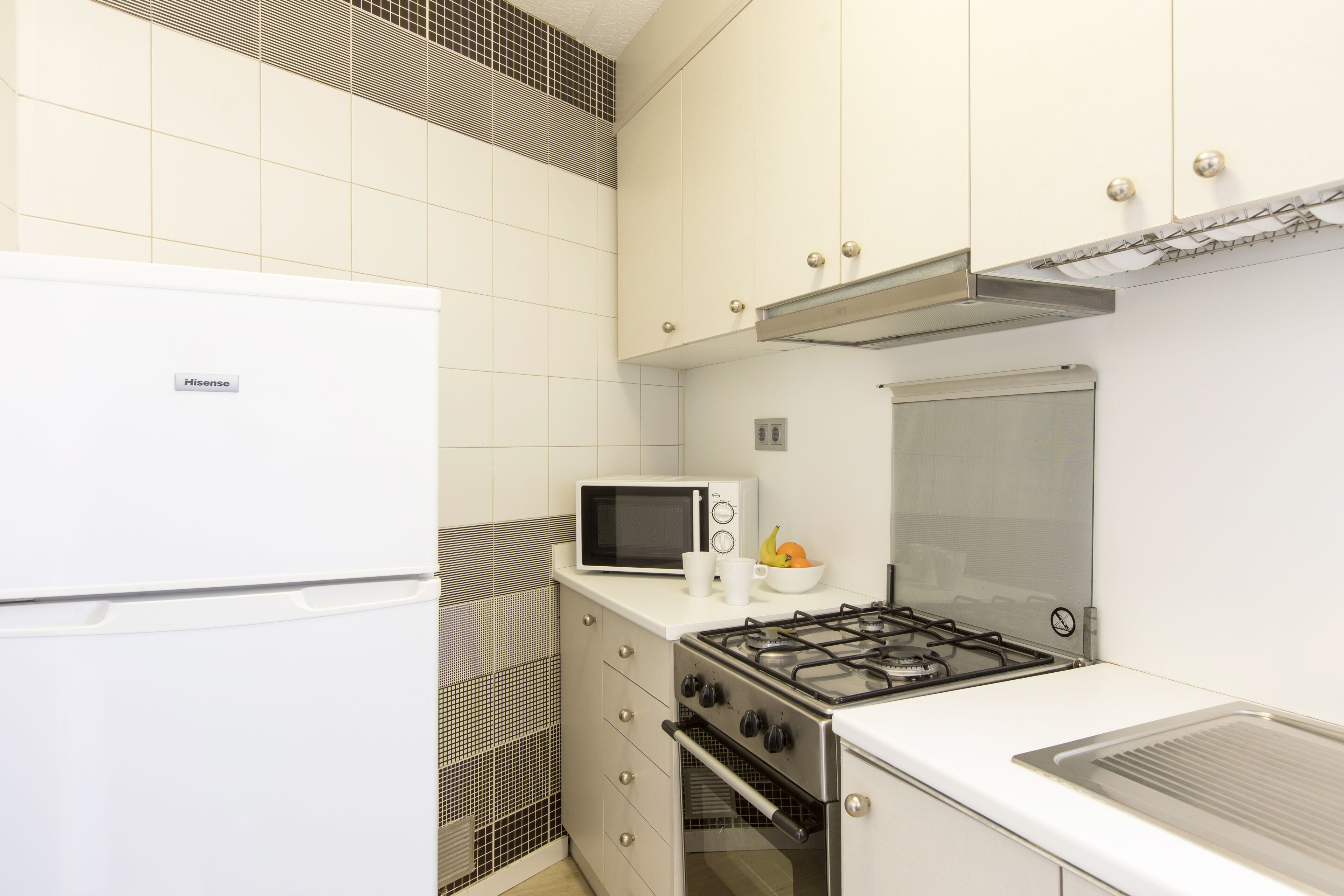 A compact kitchen with a white refrigerator, a microwave, a stove, and a sink.