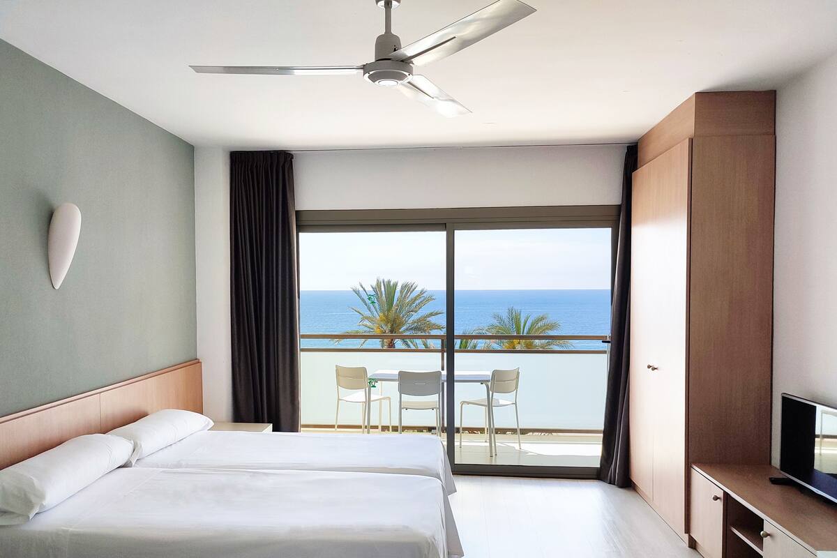 A hotel room with a balcony, a bed, a TV, and a ceiling fan.