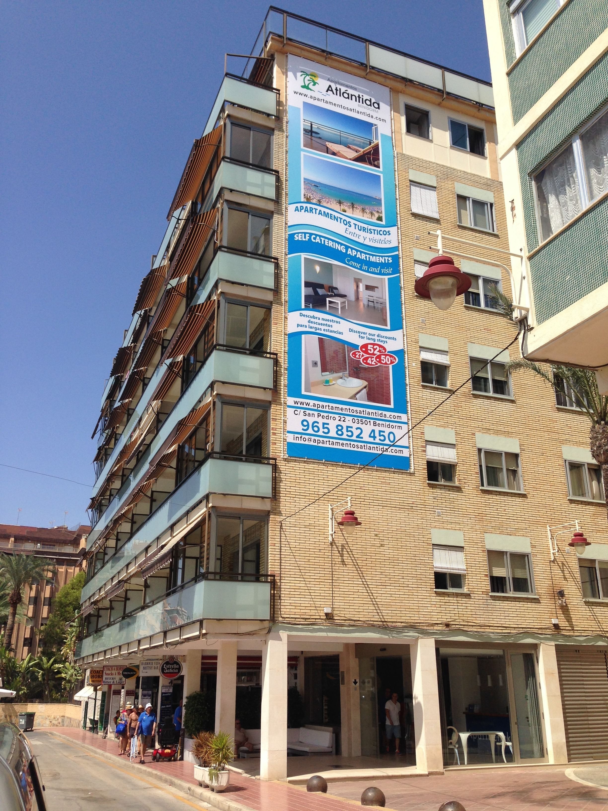 Un immeuble à plusieurs étages sur lequel est affichée une grande publicité pour un hôtel, avec une vue sur la plage, un numéro de téléphone et l’adresse de son site web.