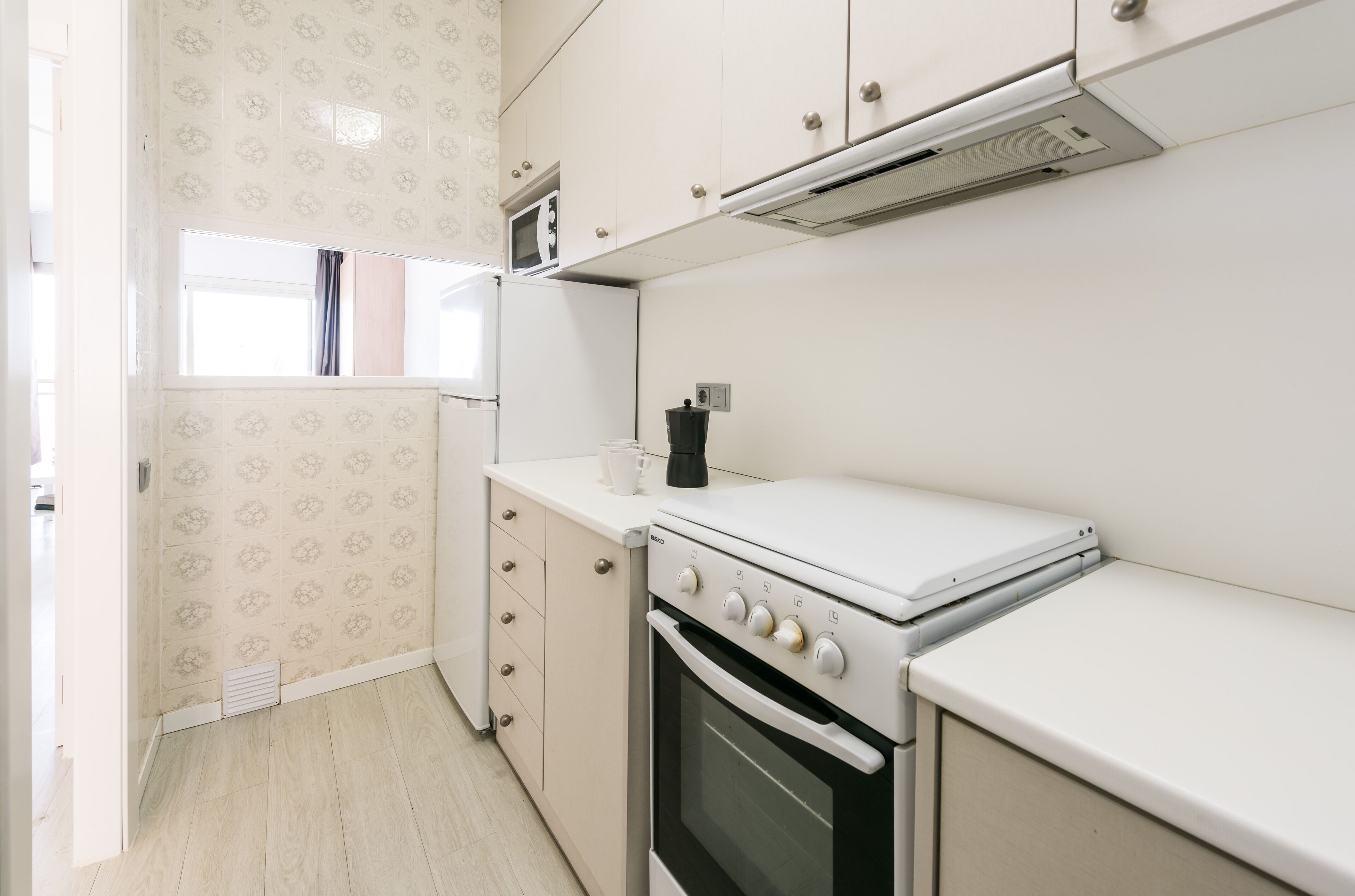A kitchen with white cabinets, a microwave, a stove, and a window with curtains.