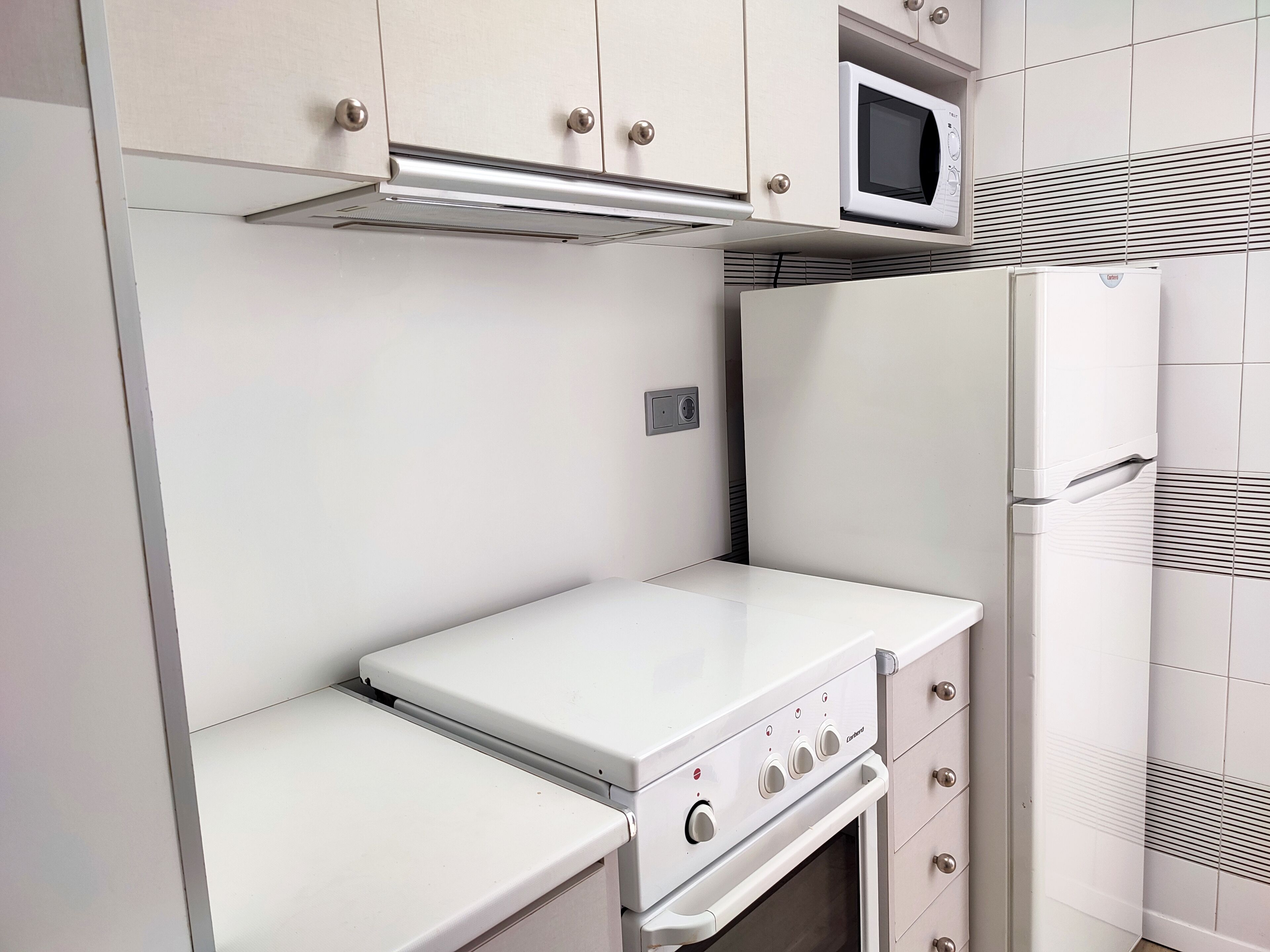 Eine kompakte Küche mit integriertem Mikrowellenherd, Backofen und kleinem Kühlschrank.